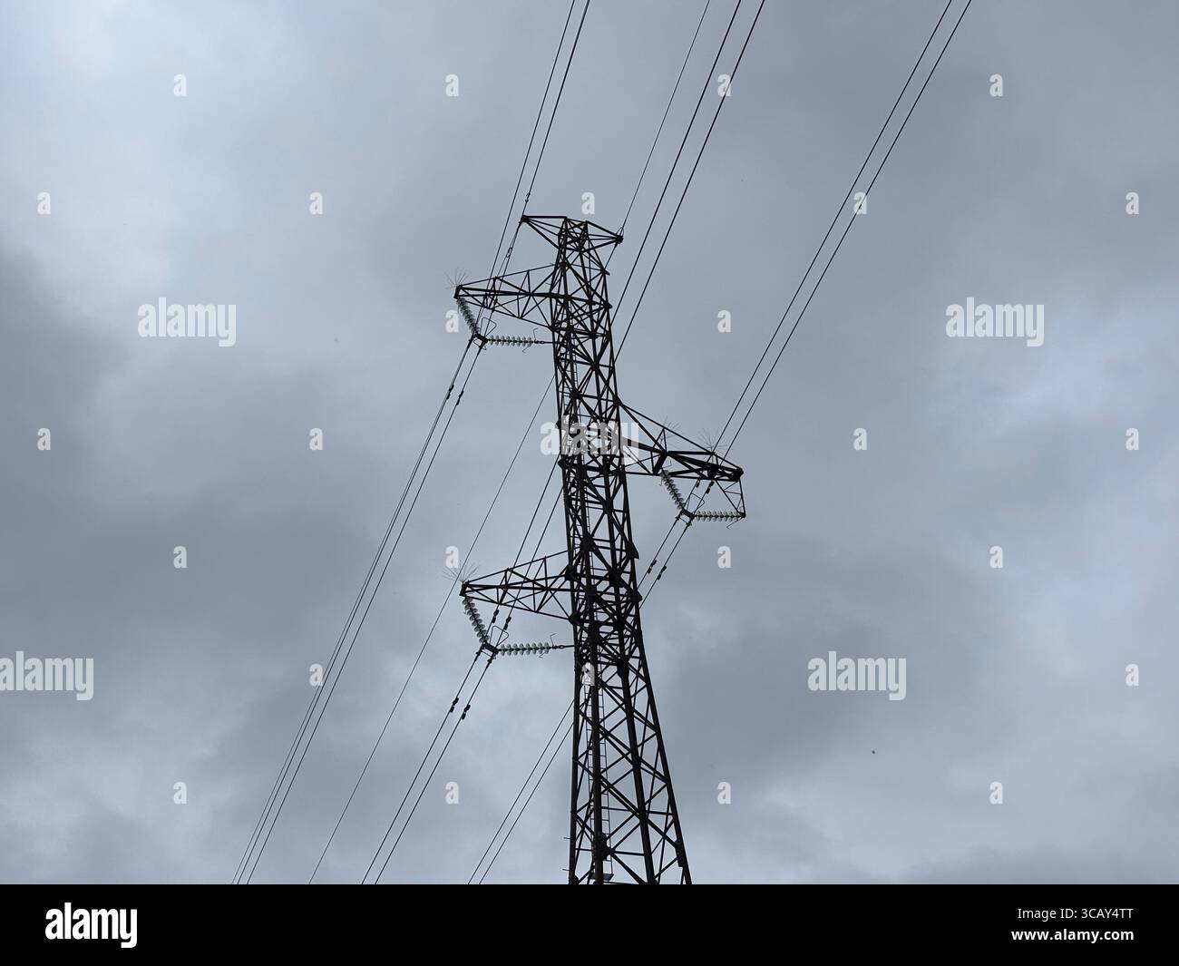 Electricity cables and electricity pylons against a grey cloudy sky. - Smartphone Captured Stock Image