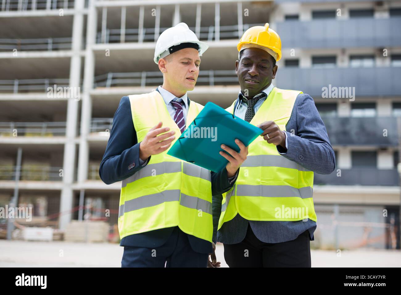 Engineer standing with builder supervising the construction process with house drawings on structure outdoors Stock Photo