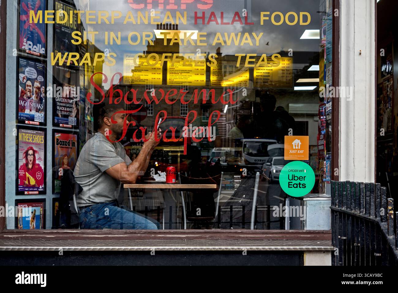 Customer sitting looking at his phone in the window of Palmyra Pizza, a takeaway restaurant specialising in pizzas and Mediterranean-style food. Stock Photo