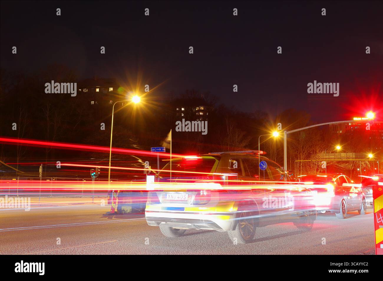 Speed light at night from cars. One Swedish police car at a red traffic light. Long exposure photo. Stock Photo