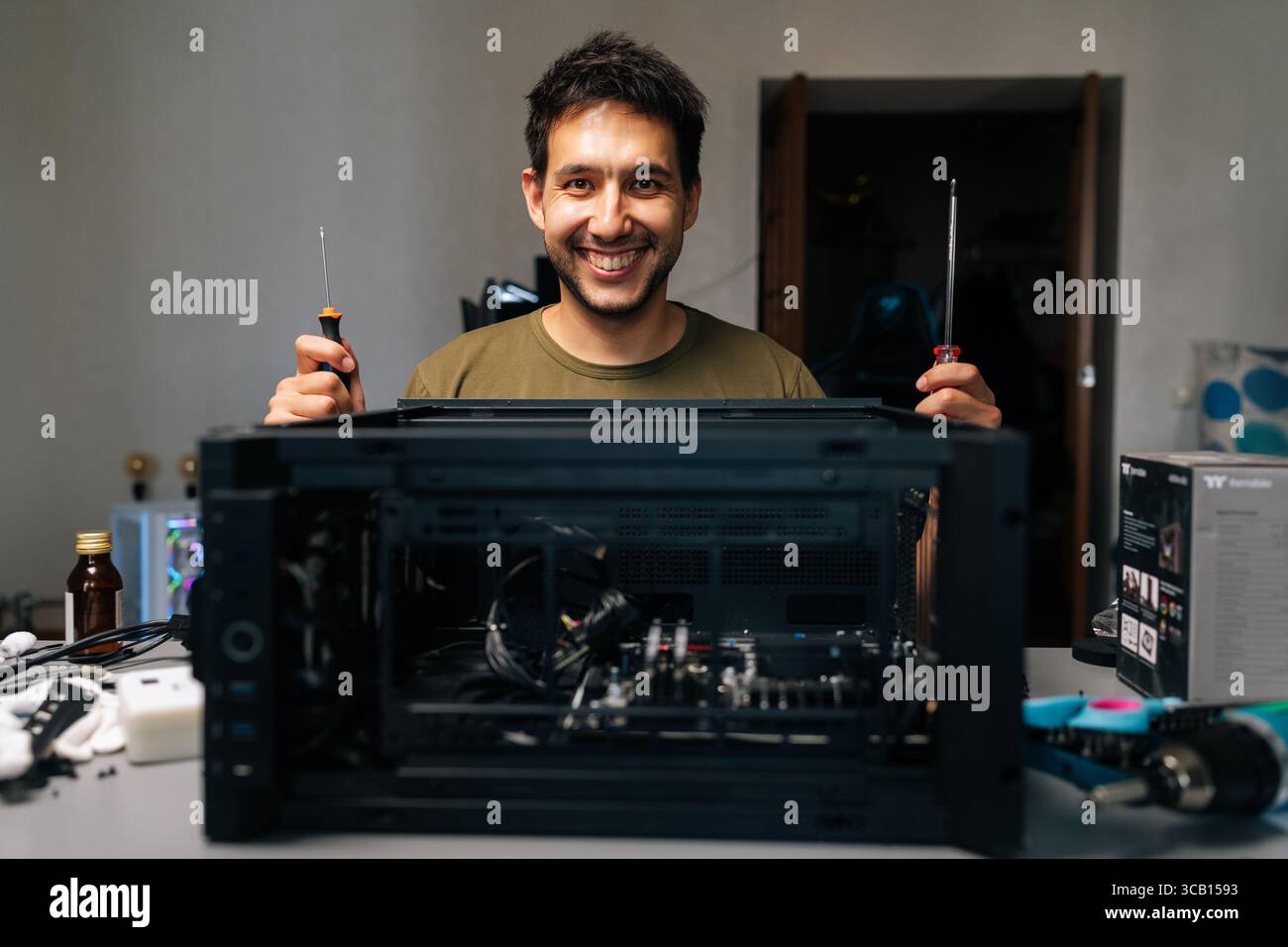 Friendly computer technician working with screwdrivers during desktop computer assembly, demonstrating technical expertise in workplace environment Stock Photo
