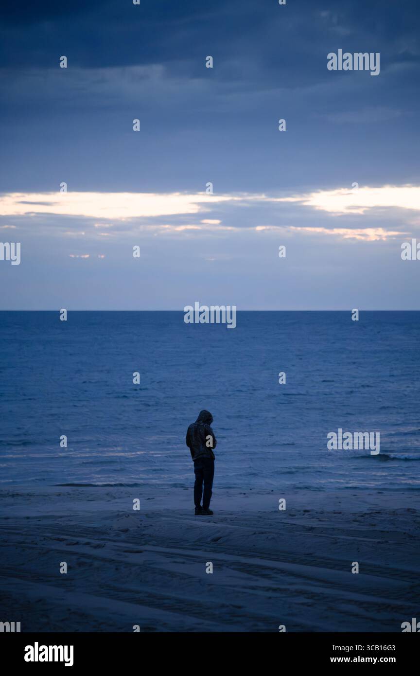 A person standing on the shore of Lake Michigan on a cloudy evening just after sunset Stock Photo