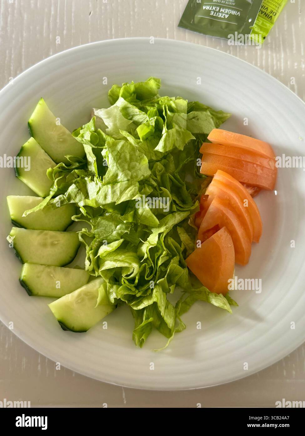 Fresh salad plate with sliced cucumber, leafy green lettuce, and sliced tomato on a white dish. - Smartphone Captured Stock Image
