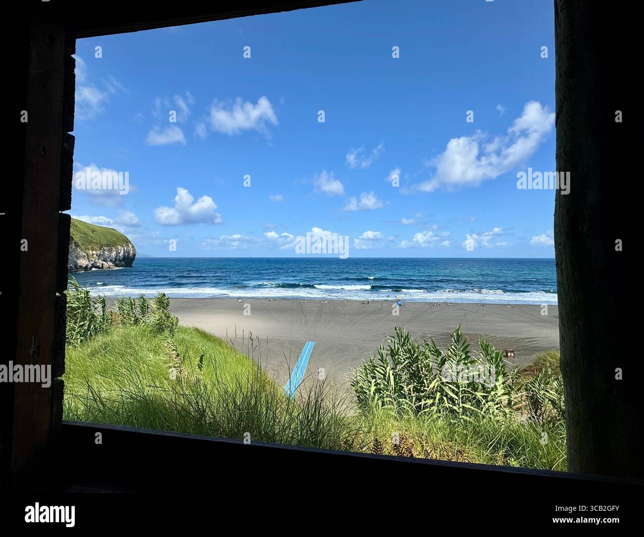 Scenic view of Santa Bárbara Beach in São Miguel, Azores, seen through a window-like frame with lush greenery and blue skies. - Smartphone Captured Stock Image