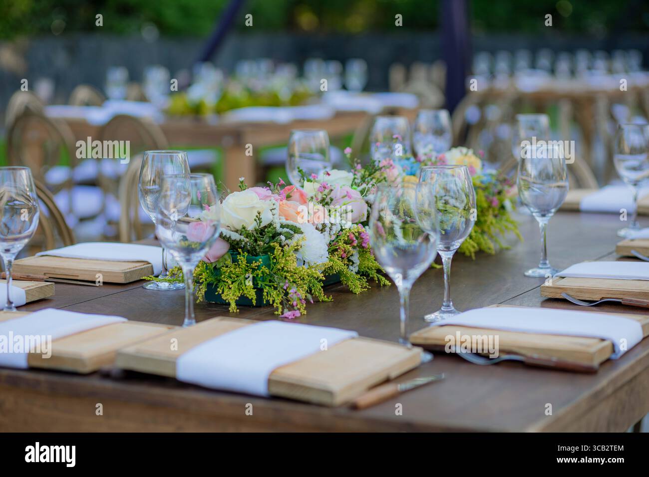 Wooden table decorated with crystal glasses and floral centerpiece, set outdoors for a wedding or elegant celebration. Stock Photo