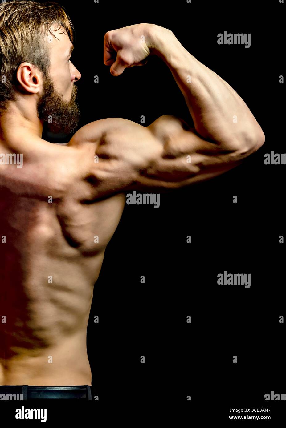 A muscular man flexes his bicep, showcasing his physique against a black background. Stock Photo