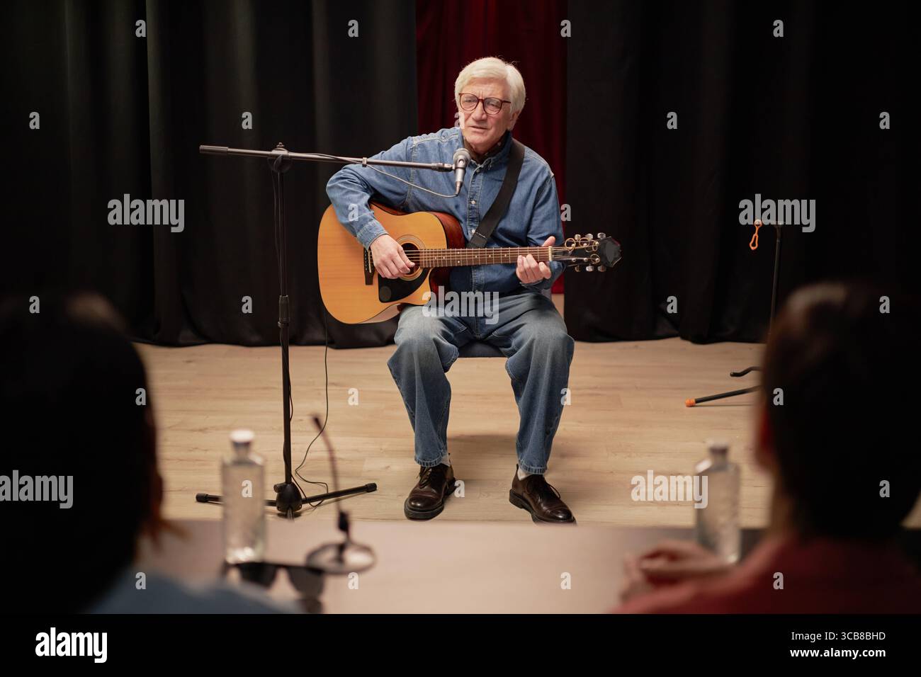Senior Man Showcasing Musical Talent with Guitar before Judges Stock Photo