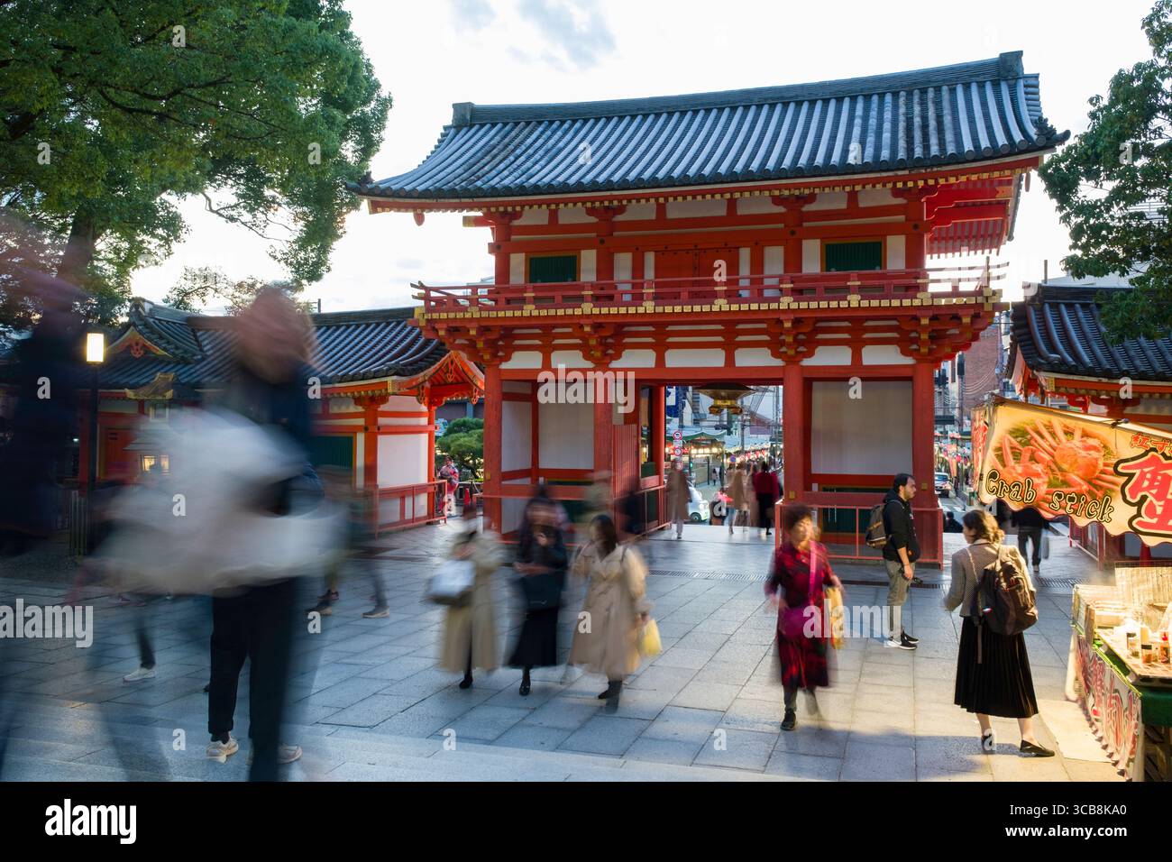 A bustling scene near Yasaka Jinja Nishiromon Gate, featuring visitors enjoying food stalls and local traditions within a peaceful and cultural ambian Stock Photo