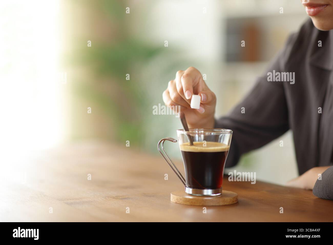 Close up of a woman hand throwing sugar cube in a coffee cup on a wooden table at home with infinite copy space Stock Photo