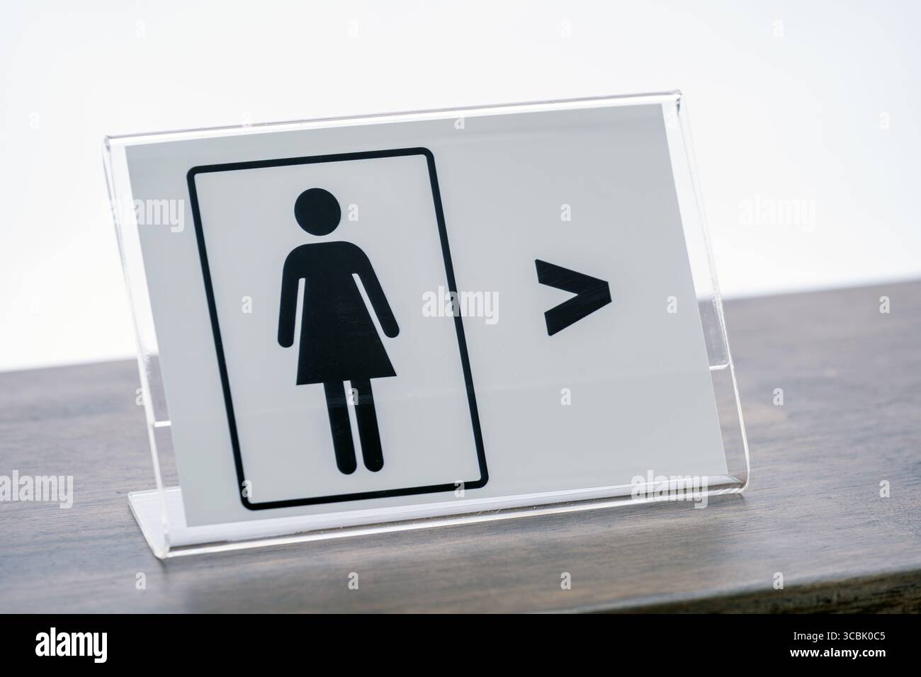 A clear acrylic sign with female restroom symbol is placed on wooden counter, indicating direction to women restroom. minimalist design Stock Photo