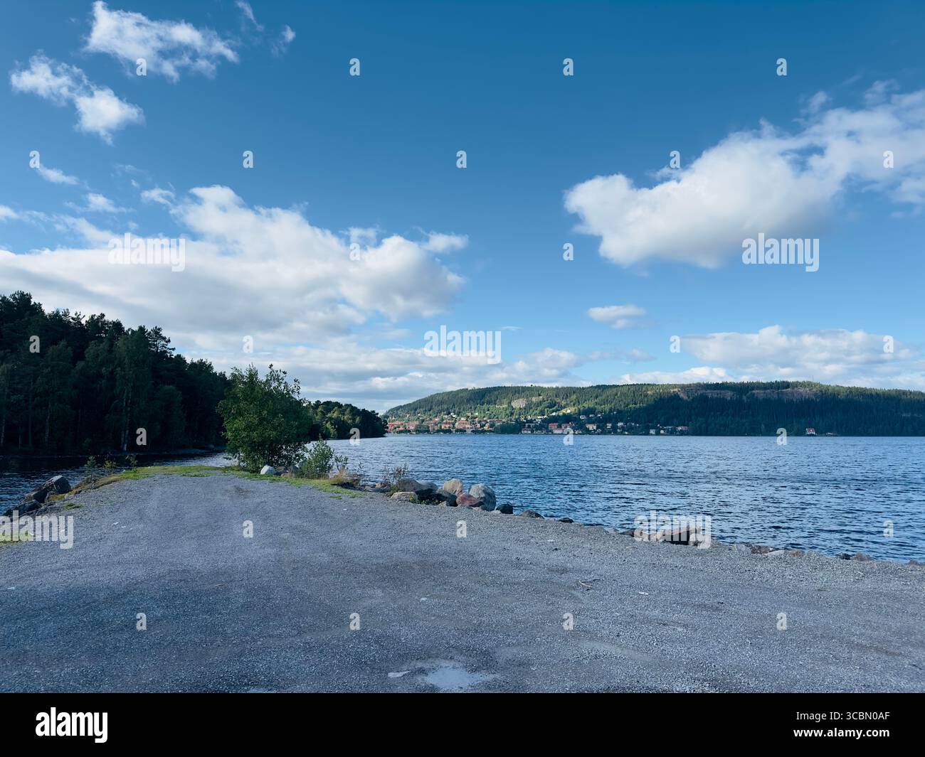 A serene lake scene with a concrete path leading to the calm water under a bright blue sky. - Smartphone Captured Stock Image