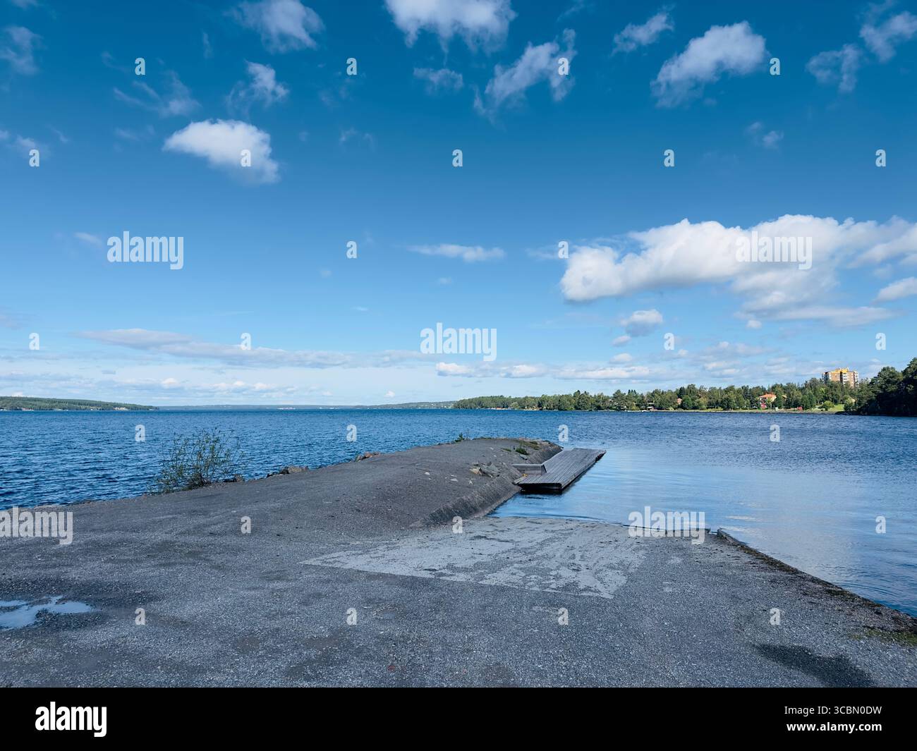 A serene lake scene with a concrete path leading to the calm water under a bright blue sky. - Smartphone Captured Stock Image