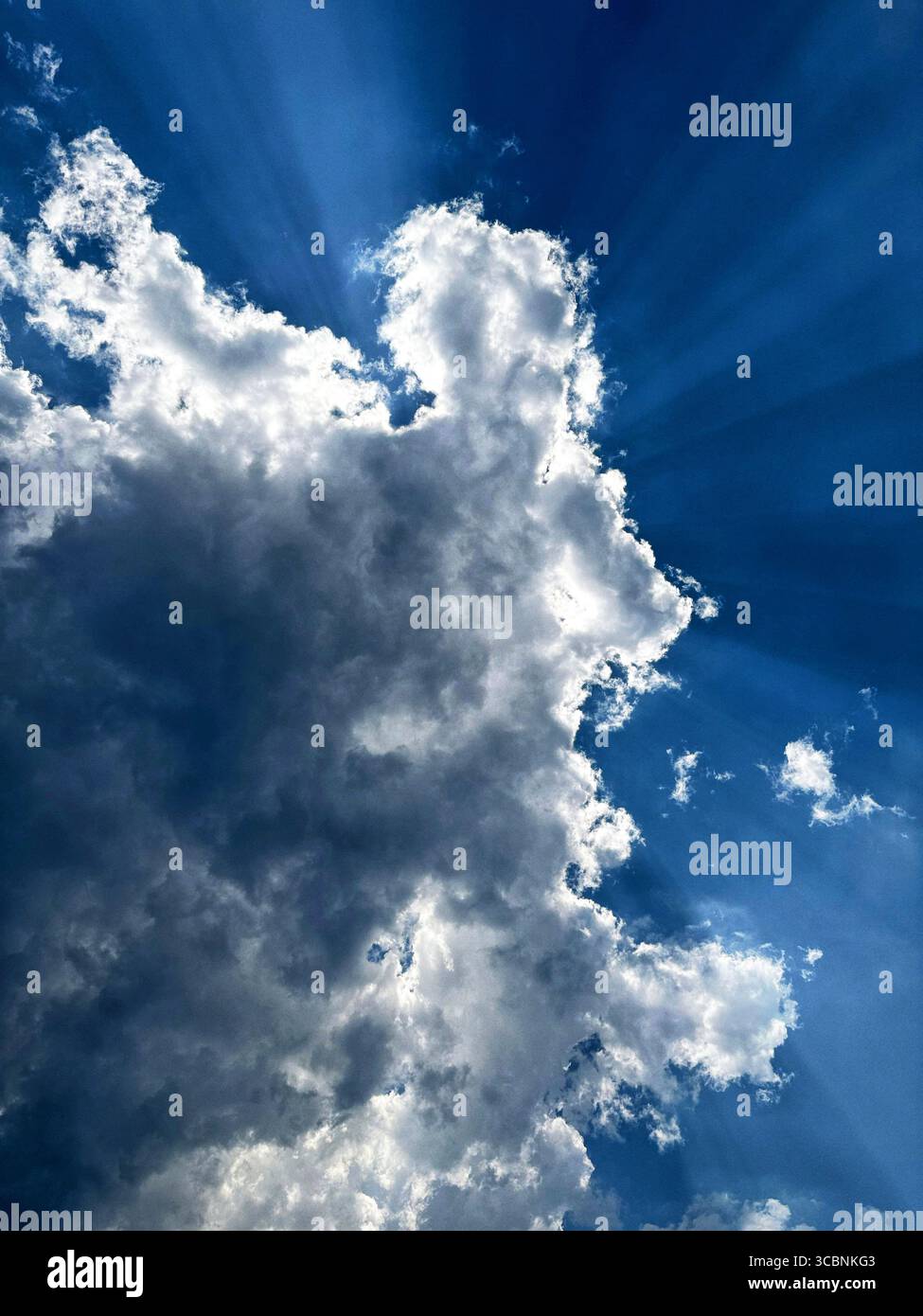 Dramatic cloudscape with sun rays bursting through dark cumulus clouds in a deep blue sky. Stock Photo