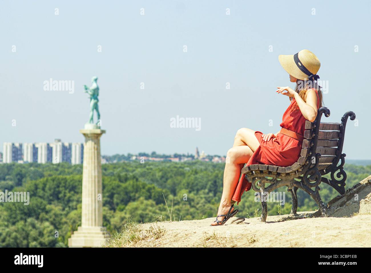 Carefree summer moment in Belgrade: a woman in a bright dress and sunhat rests on a bench at Kalemegdan. Relaxed holidays and urban exploration Stock Photo
