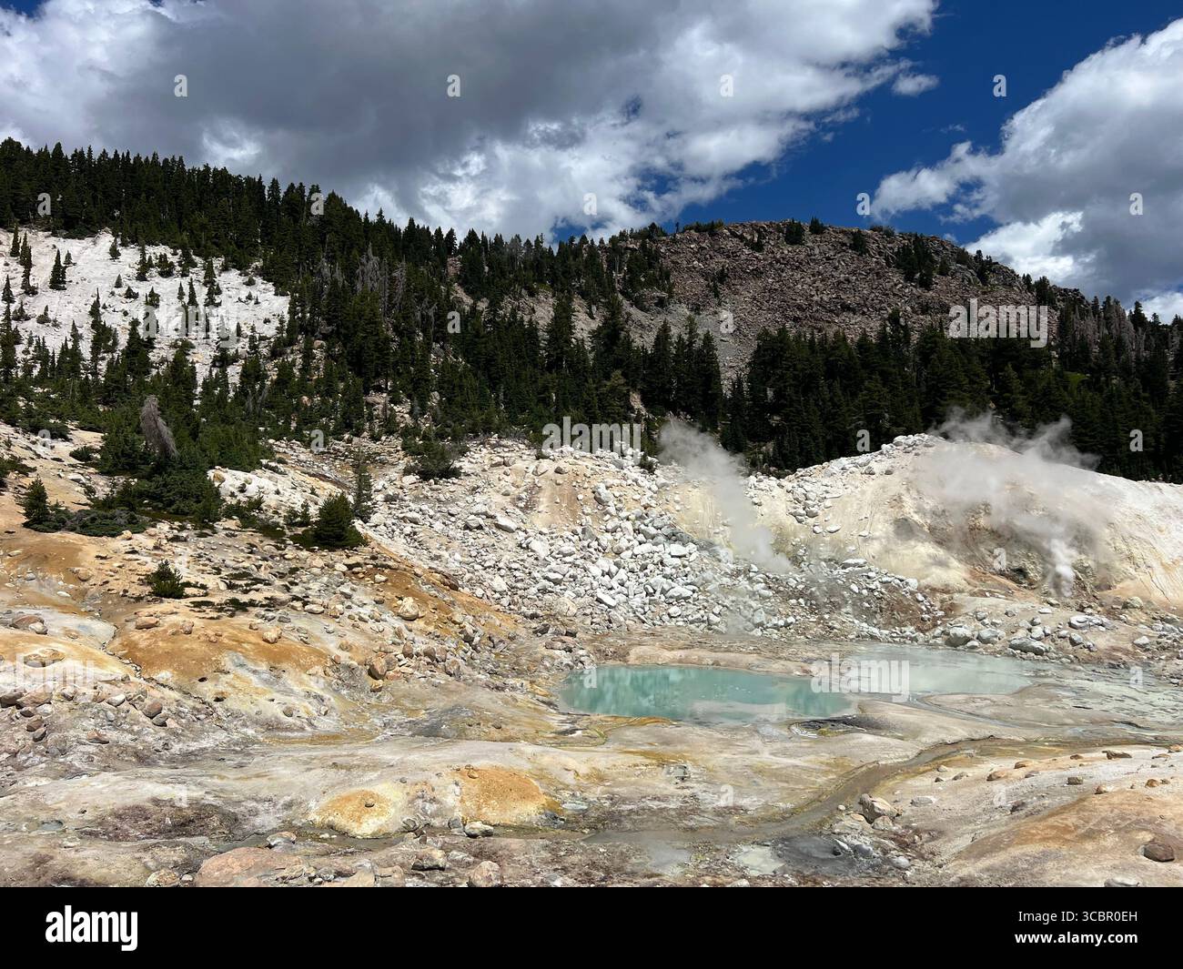 Geothermal pool and fumaroles at Bumpass Hell in California with colorful rocks, steam, and dramatic skies over volcanic terrain. - Smartphone Captured Stock Image