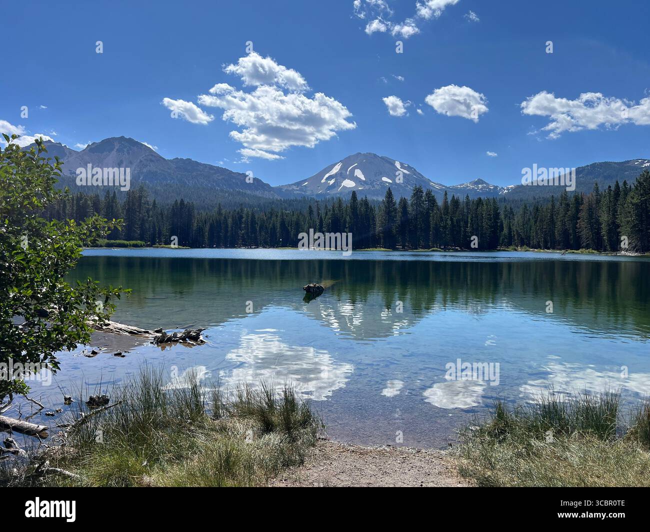 Summer view of Manzanita Lake reflecting Lassen Peak with snow-capped summit under blue sky, Lassen Volcanic National Park, California, USA. - Smartphone Captured Stock Image