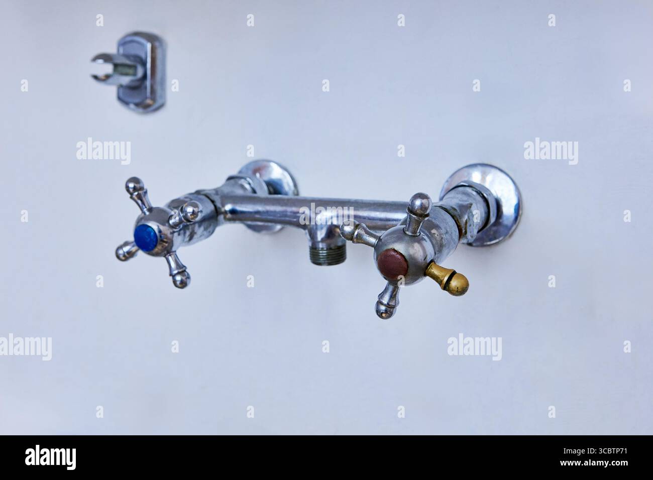 Old kitchen tap with cross handle valves and removed spout mounted on wall awaiting dismantling. Stock Photo