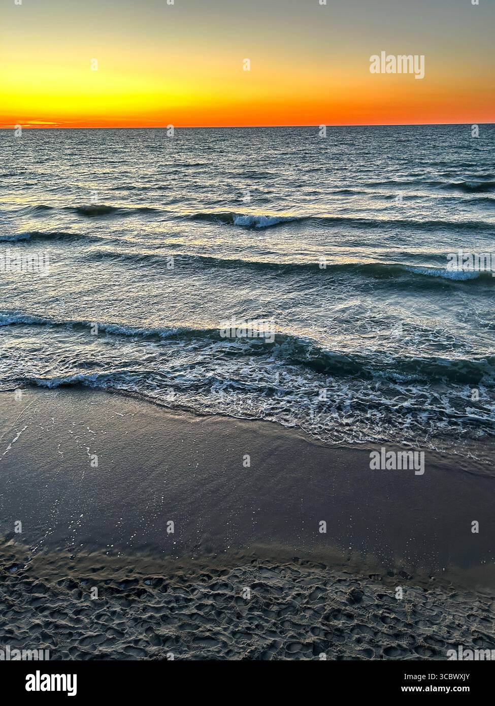 Sunset gradient from blue to orange above blue ocean water with small waves. Stock Photo