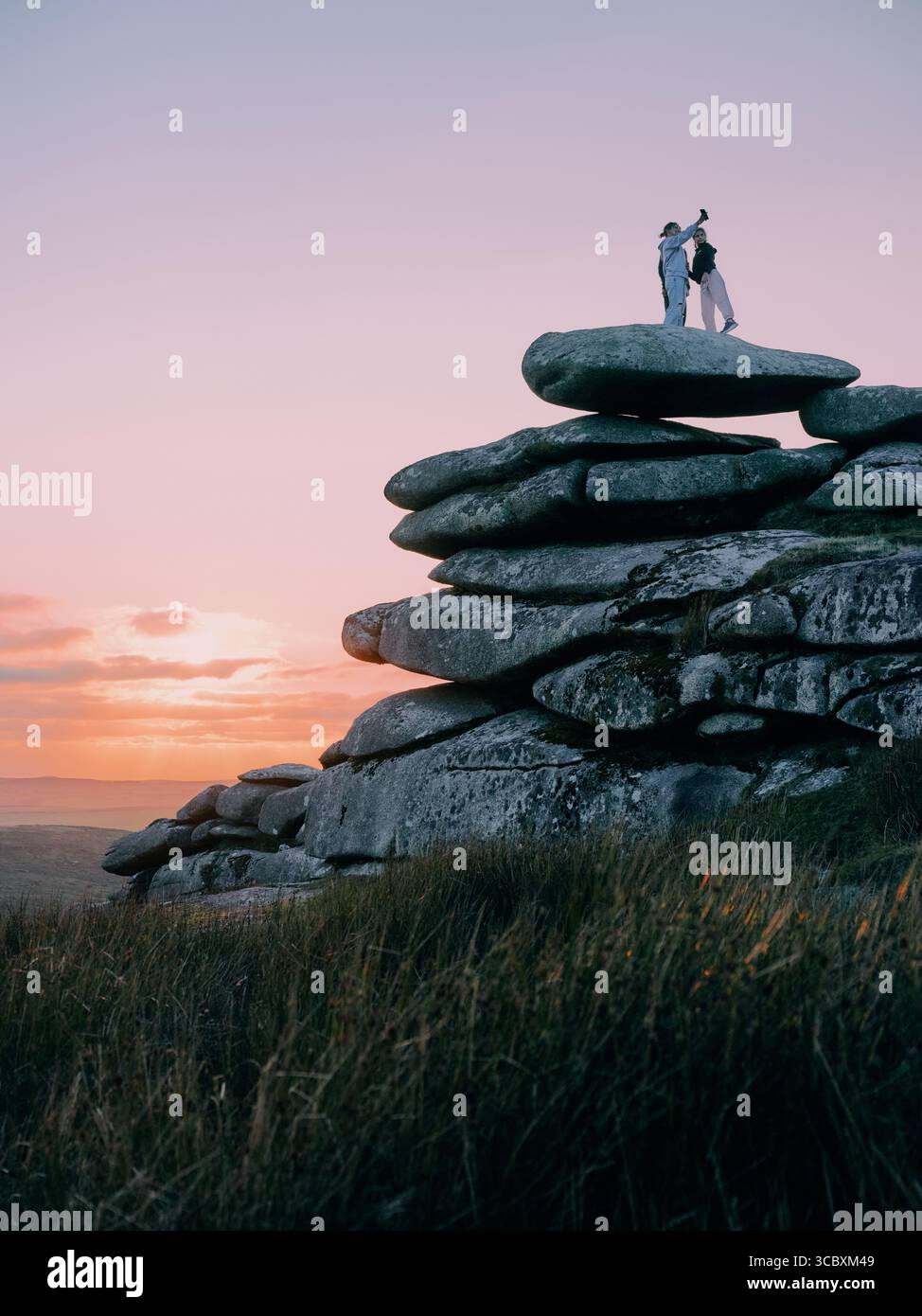 Figures enjoying the sunset on the granite tor on Stowes Hill, Minions, Bodmin Moor, Cornwall England UK Stock Photo
