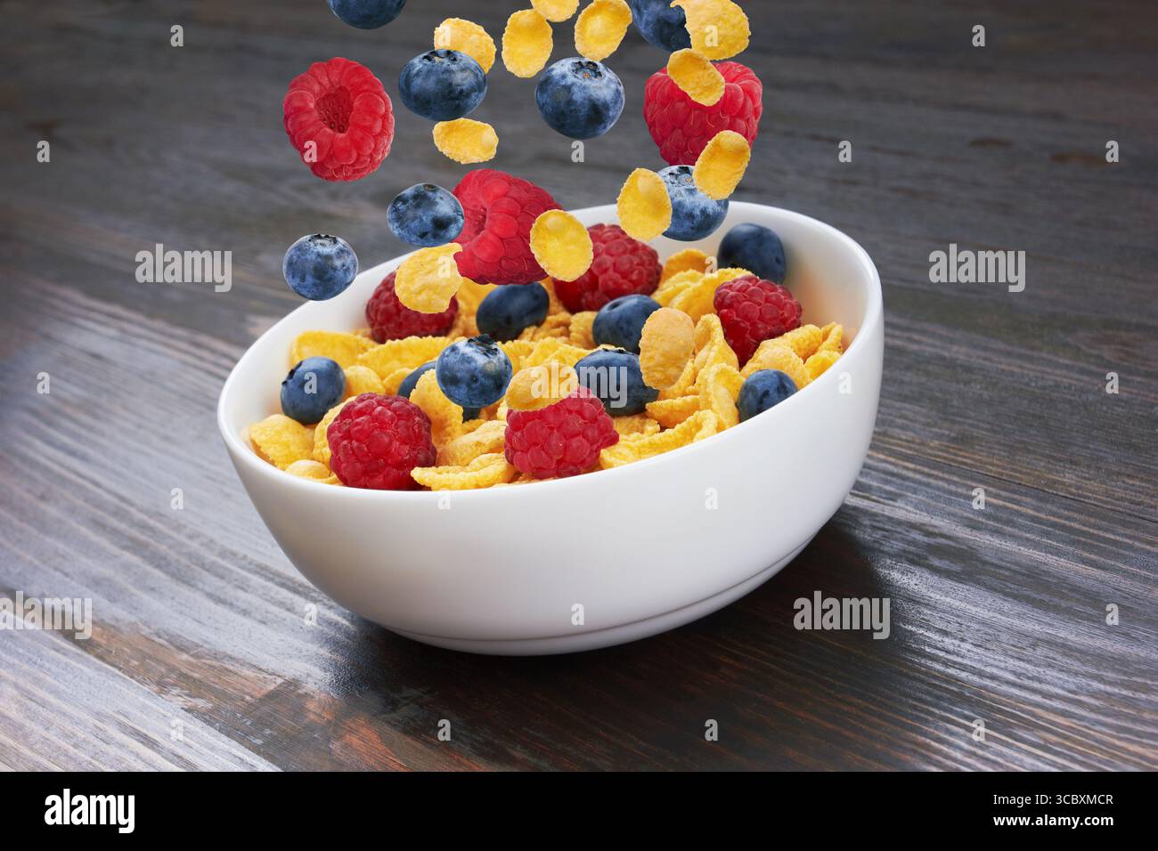 Falling fresh berries in corn flakes, on wooden background Stock Photo