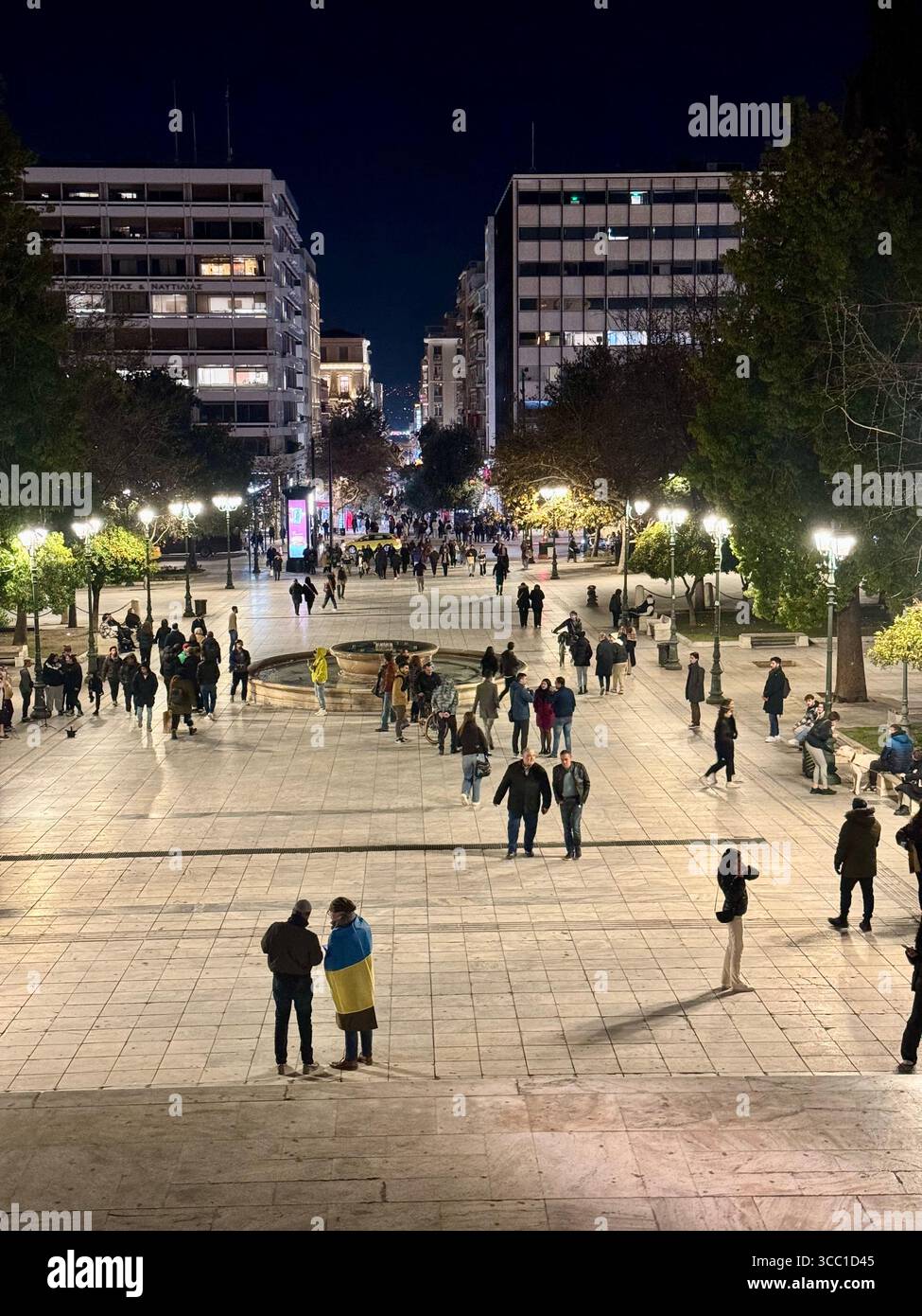 Nighttime view of Syntagma Square in Athens, Greece, with illuminated streets and people walking. - Smartphone Captured Stock Image