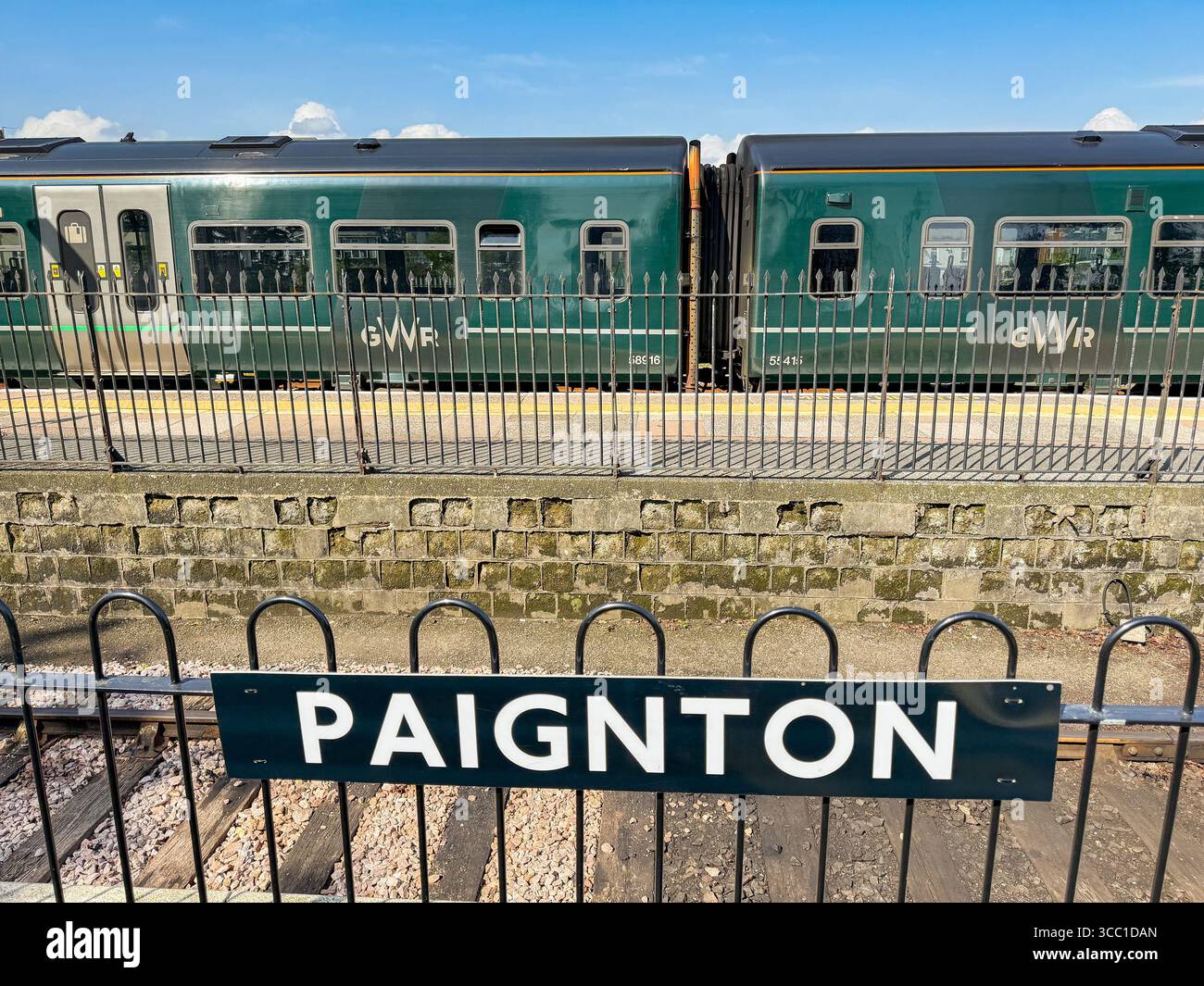 Paignton, Devon, England, UK - 24 April 2025: Station name sign on a platform at Paignton Railway Station with a Great Western Railway GWR train - Smartphone Captured Stock Image