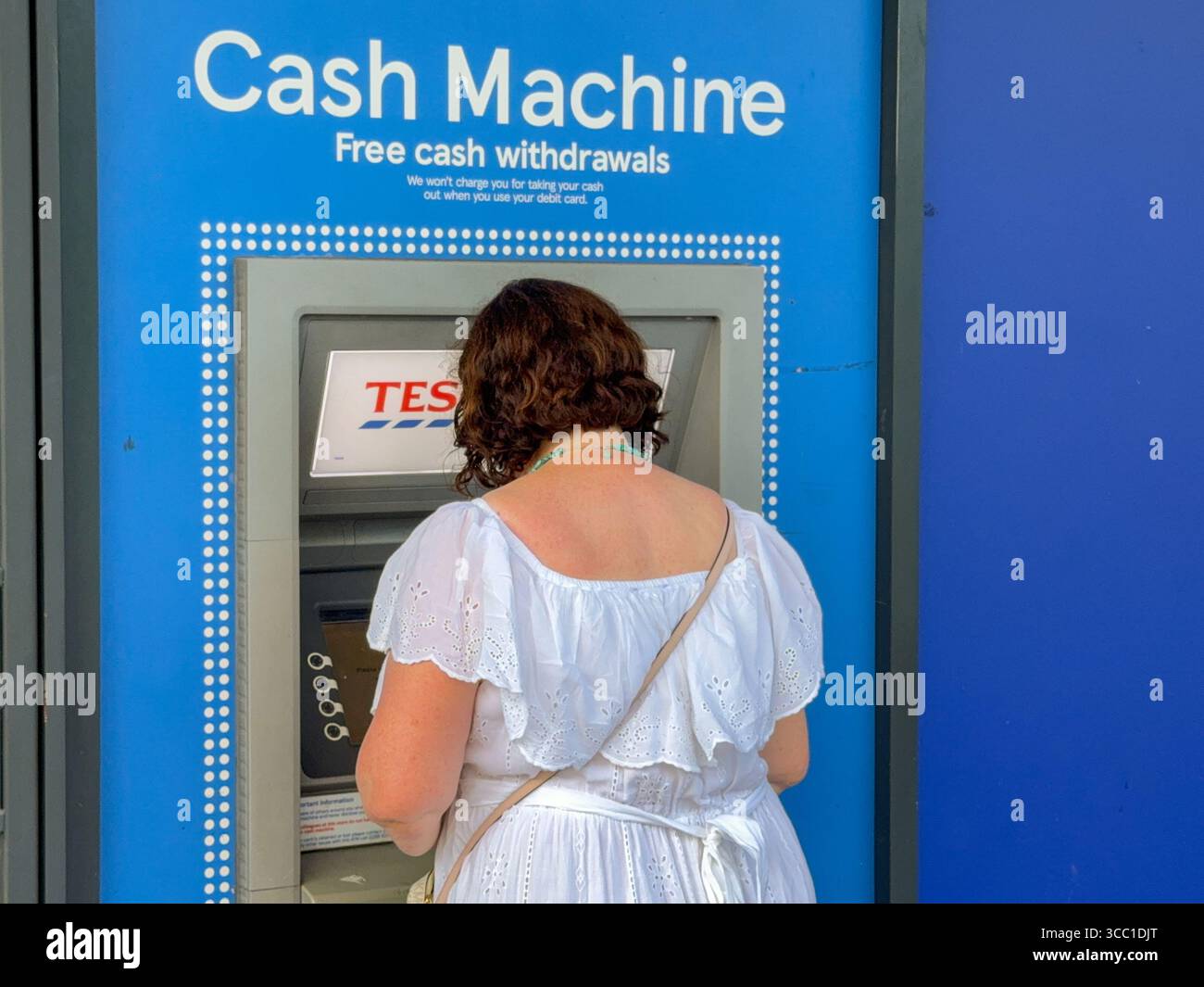 Pontypridd, Wales, UK - 12 July 2025: Person withdrawing money from a cash machine outside the branch of Tesco Express in Pontypridd town centre - Smartphone Captured Stock Image