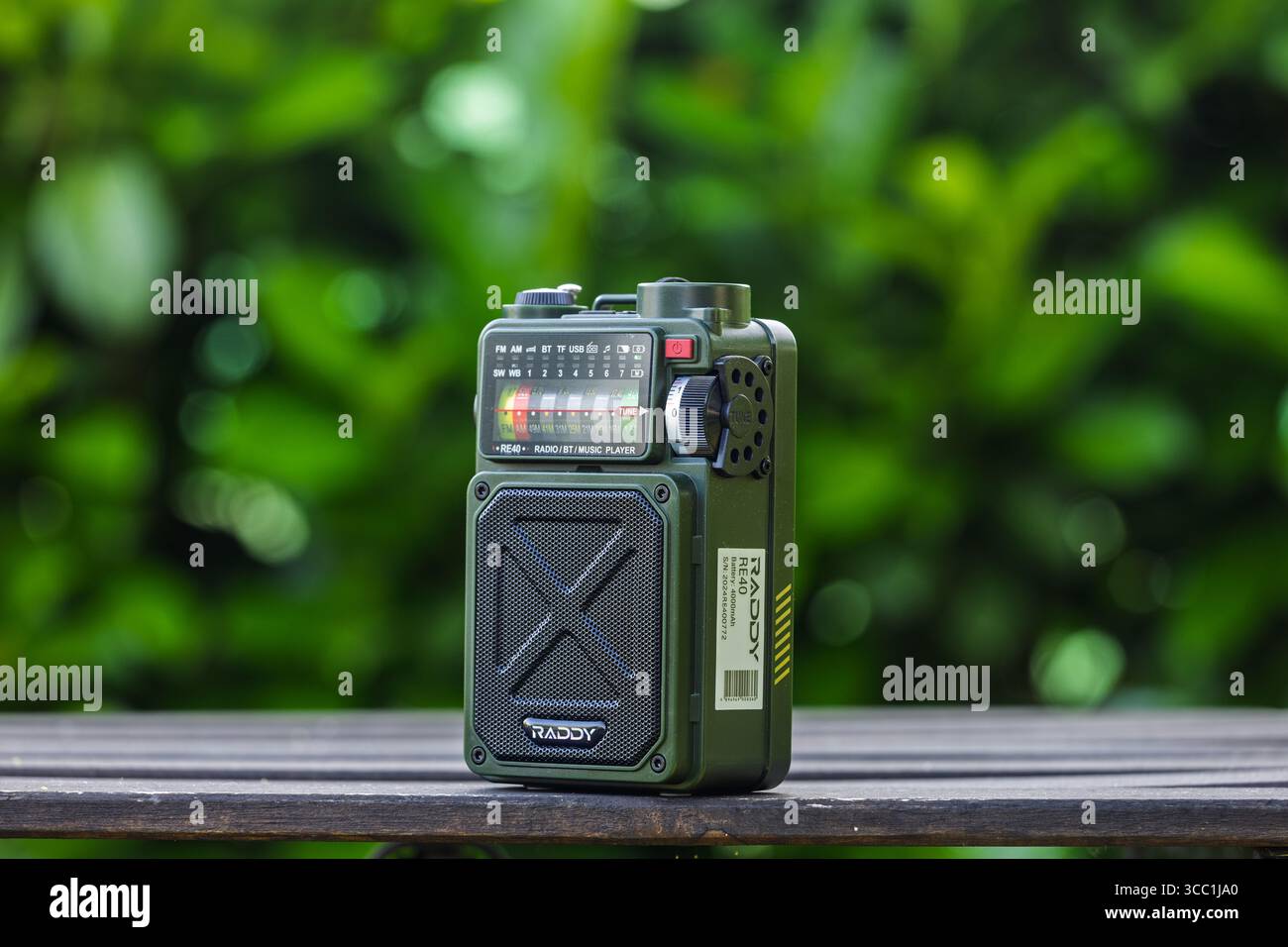 VINKOVCI, CROATIA, 06.13.2025:Compact portable radio player with a retro design placed on a wooden table outdoors. Green foliage provides an aesthetic Stock Photo