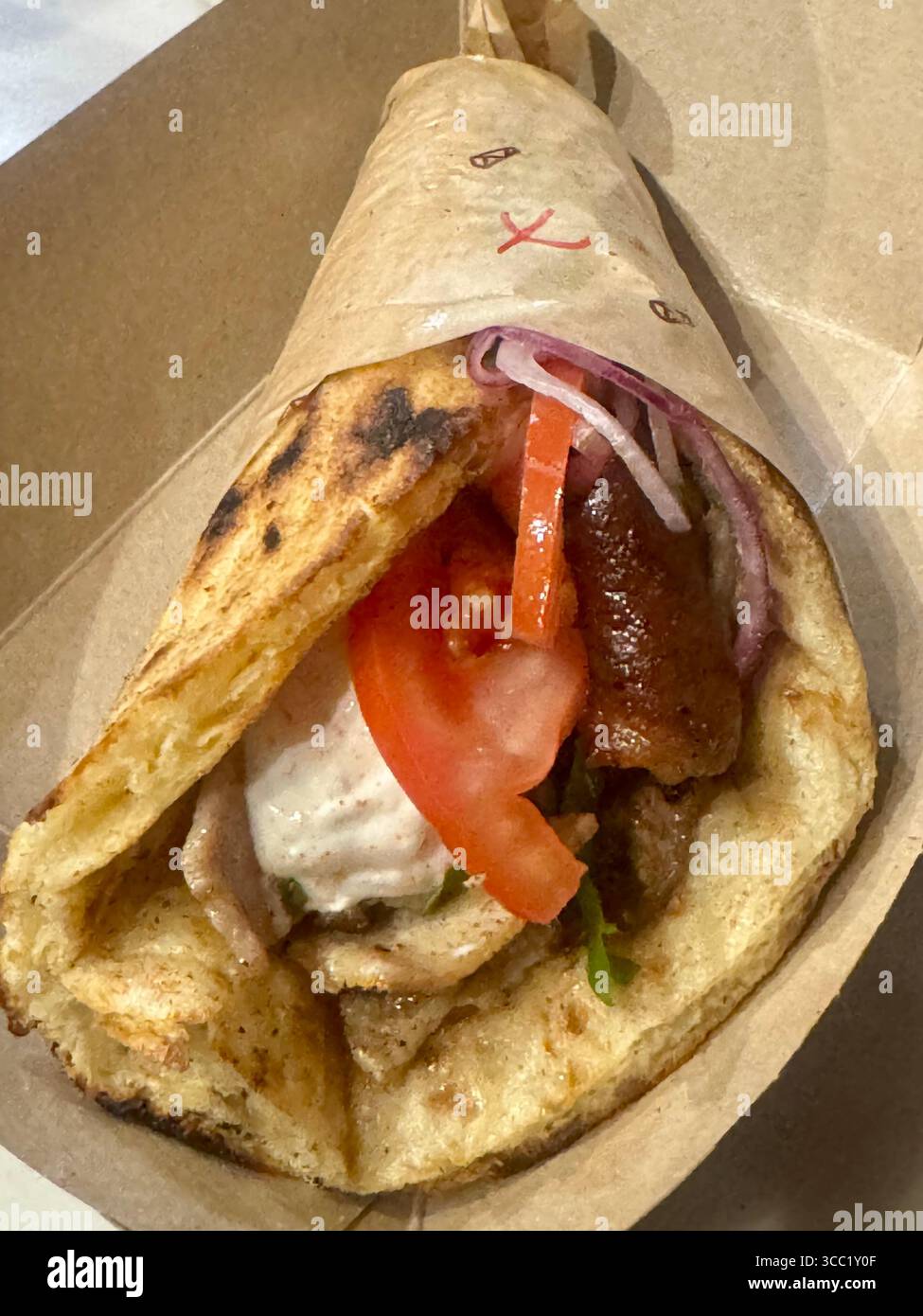Traditional Greek pork gyro in grilled pita with tomato, onion, and tzatziki sauce. - Smartphone Captured Stock Image