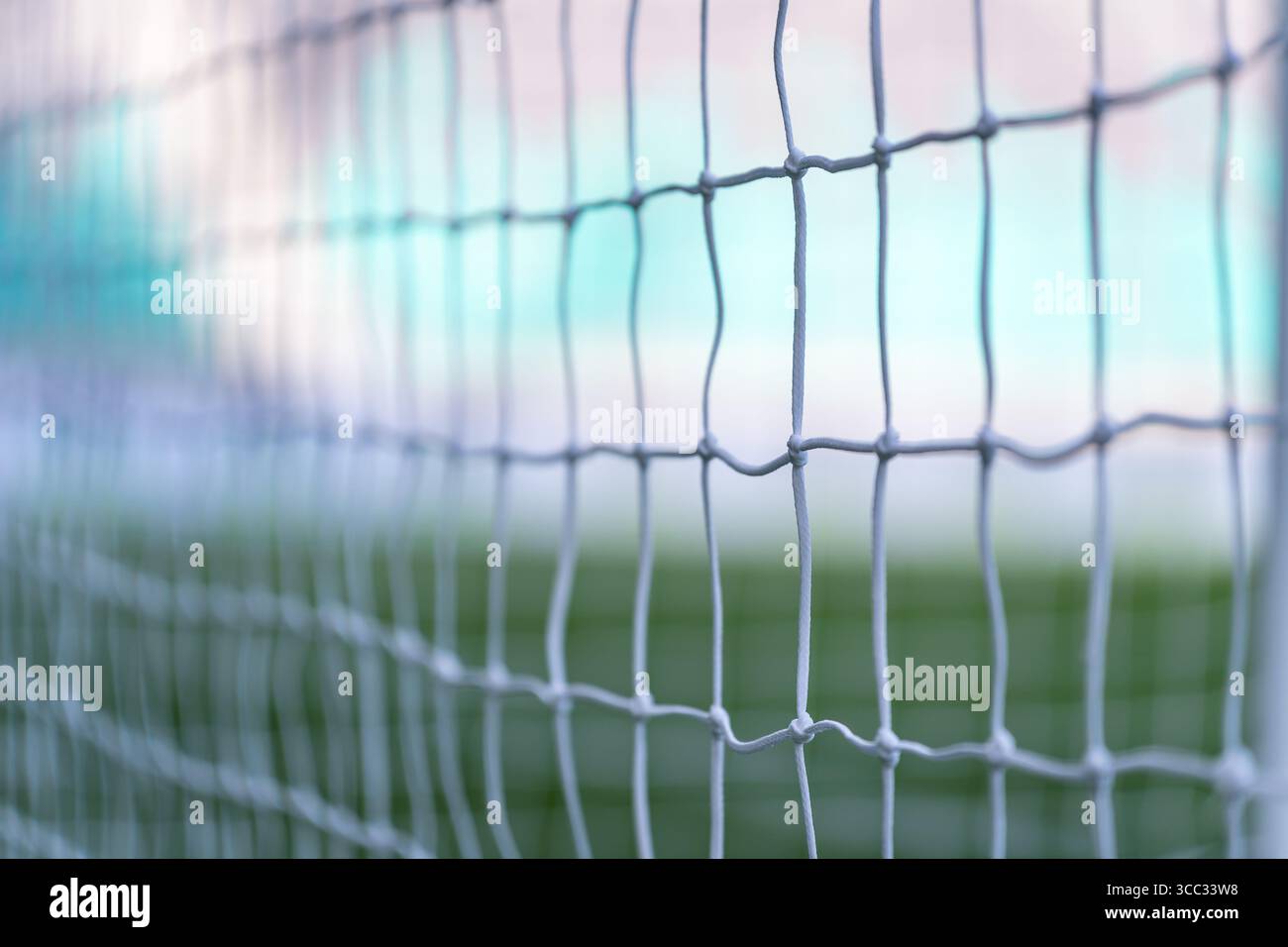 Soccer goal net close-up with blurred field and stadium, creating an abstract sporting background Stock Photo