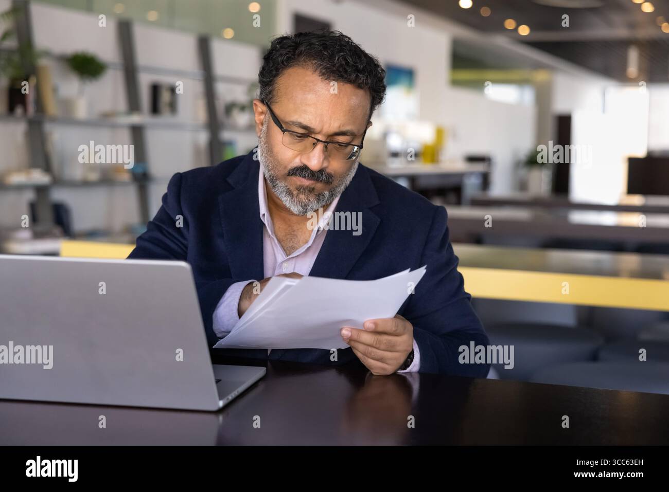 Serious focused elder Indian executive man reading document carefully Stock Photo