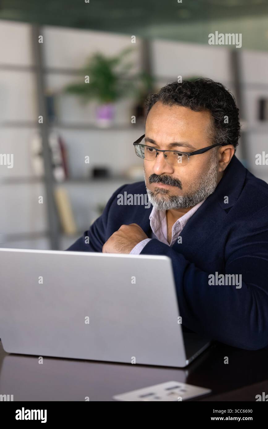 Serious older Indian business professional man working at laptop computer Stock Photo