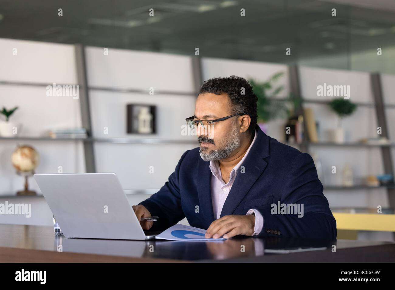 Serious busy elder Indian executive using online business application Stock Photo