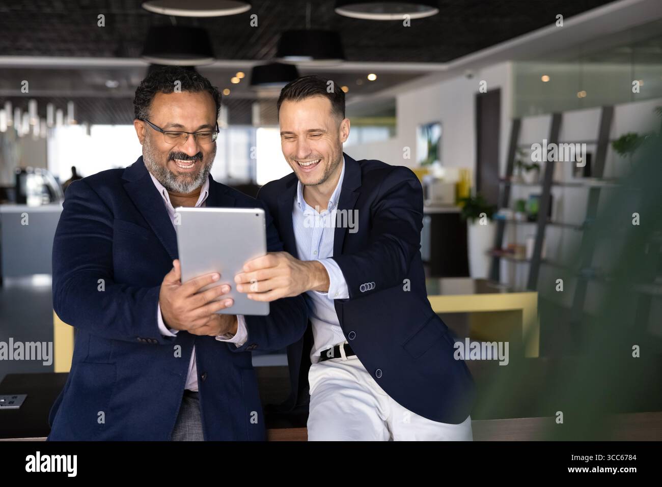 Two excited younger and elder office colleagues using digital tablet Stock Photo