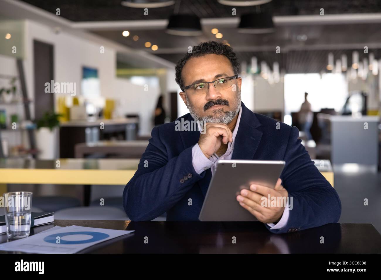 Thoughtful old Indian business man working with tablet in co-working Stock Photo