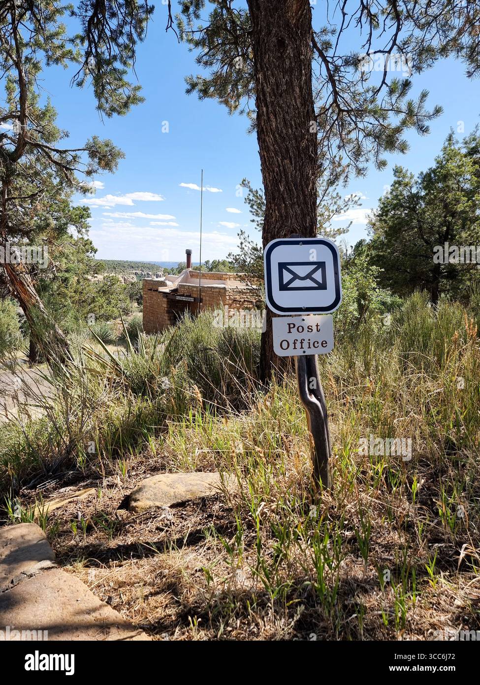 Post office sign with text and letter icon / pictogram on a curved pole in rural area with tree & high grass in National Park in Colorado USA Stock Photo