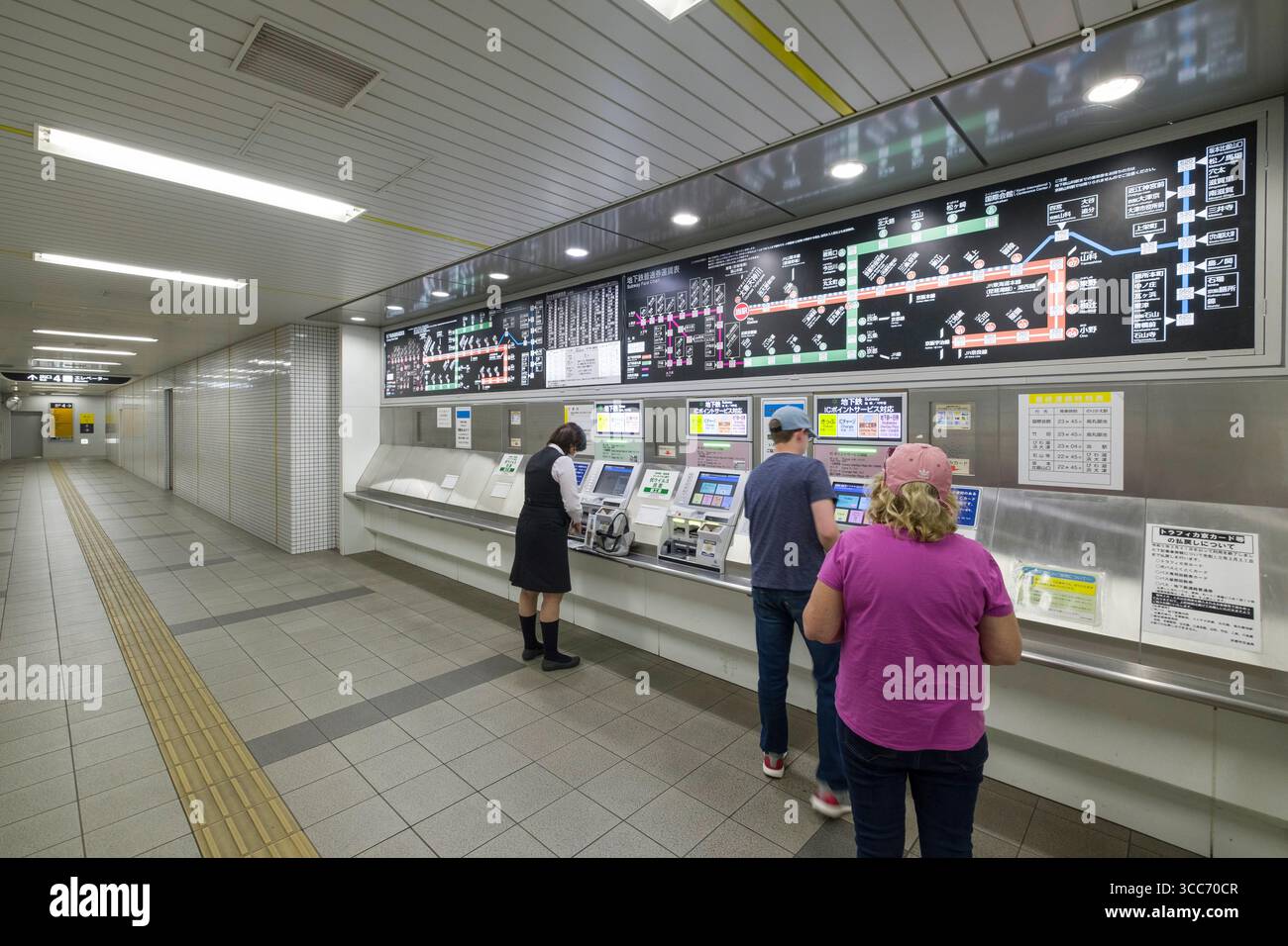 Passengers at a transport hub engage with ticket machines. The bright ...