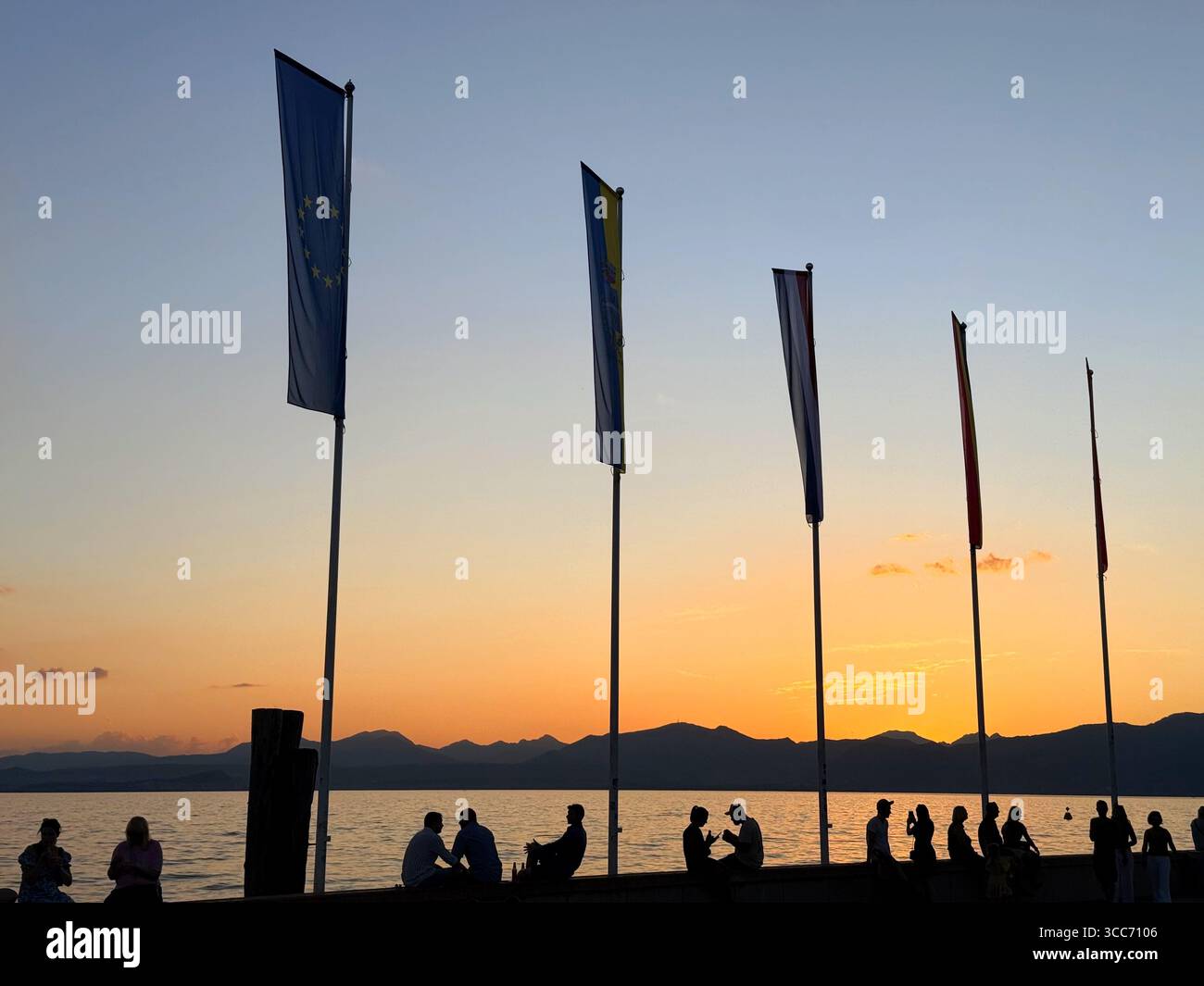 Garda on Lake Garda, Italy. People gathered on harbour by flags for the sunset. - Smartphone Captured Stock Image