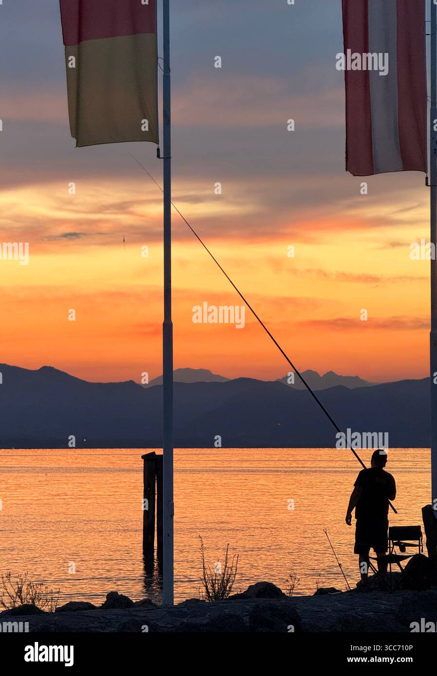 Cisano (near Bardolino) on Lake Garda, Italy. Figure in silhouette fishing from harbour at sunset - Smartphone Captured Stock Image