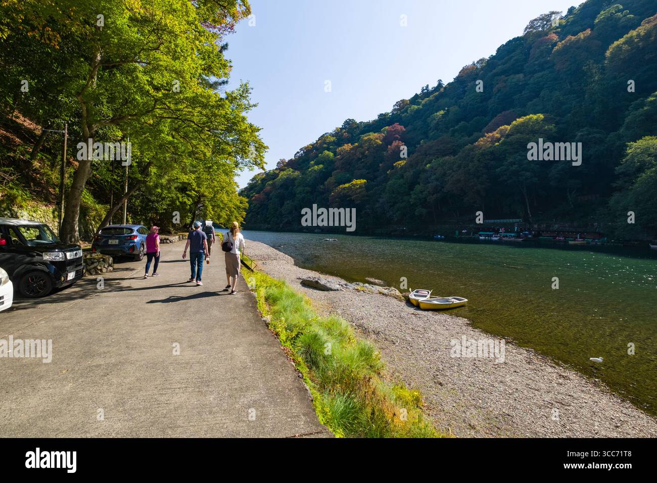 A group of people walking along a riverside path surrounded by lush ...