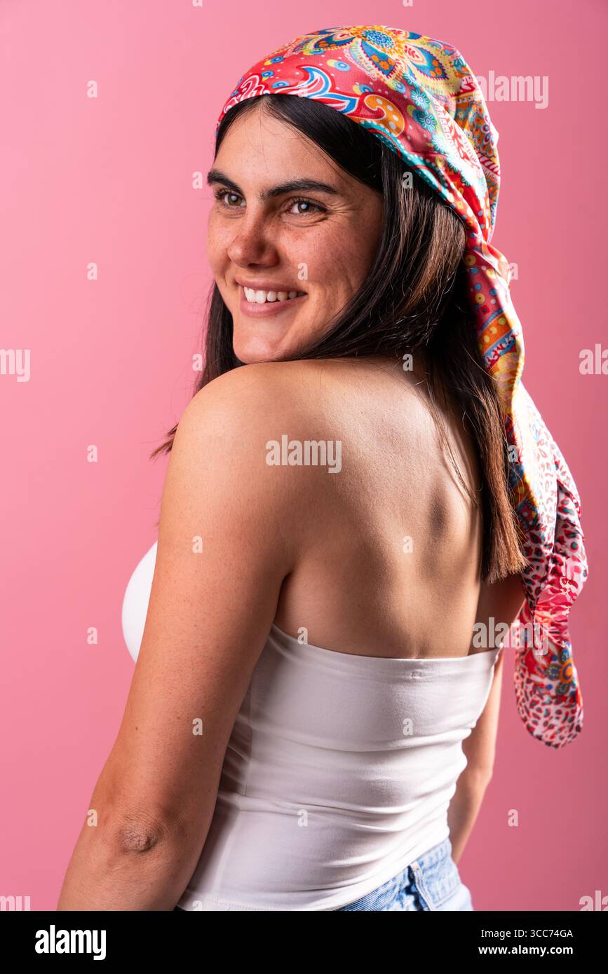 Portrait of a young woman showcasing her unique style with a colorful headscarf. Her confident smile and tattoos add to her distinctive look against a Stock Photo