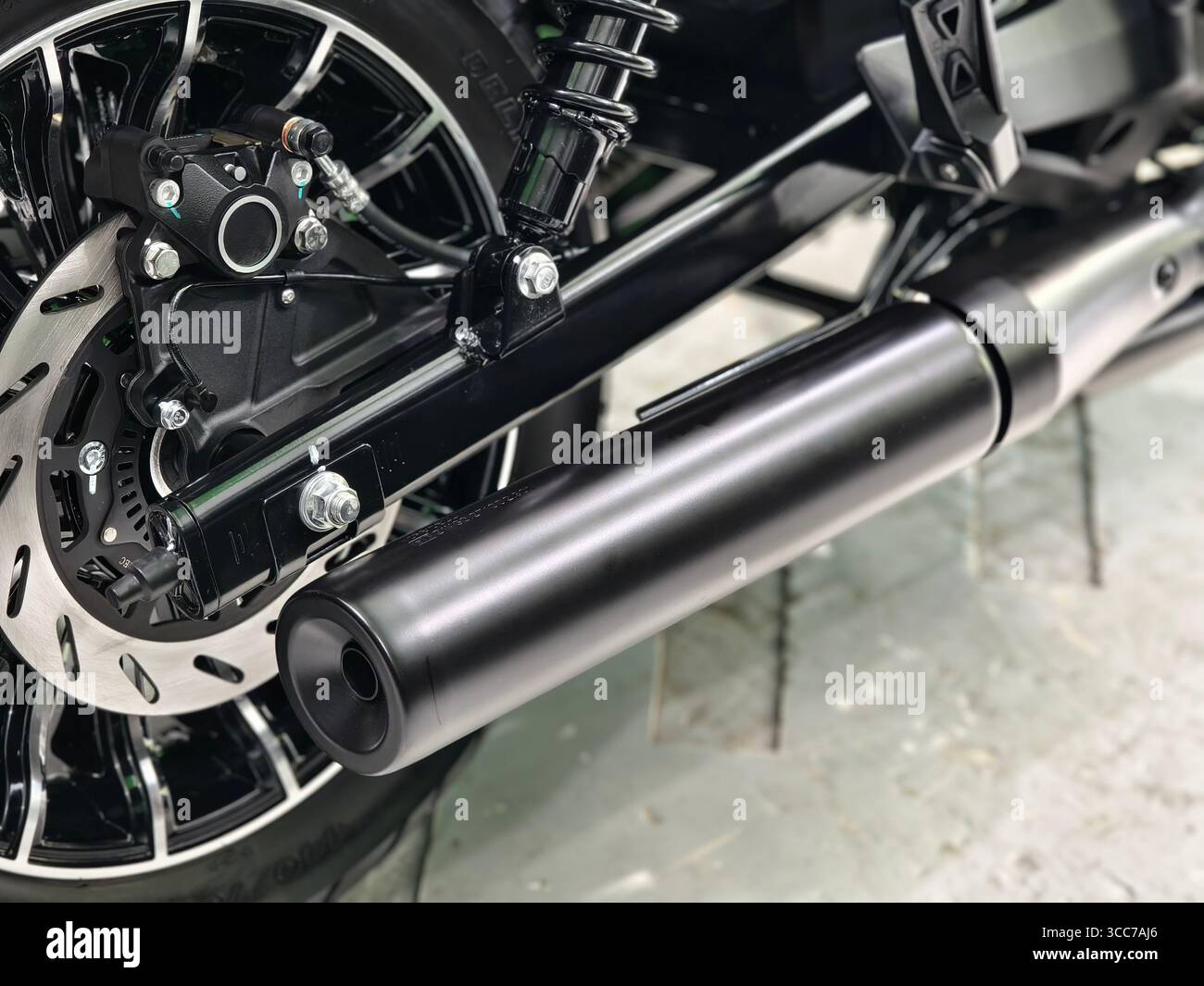 Close-Up of Motorcycle Rear Disc Brake, Caliper, Wheel, and Matte Black Exhaust Pipe System Stock Photo