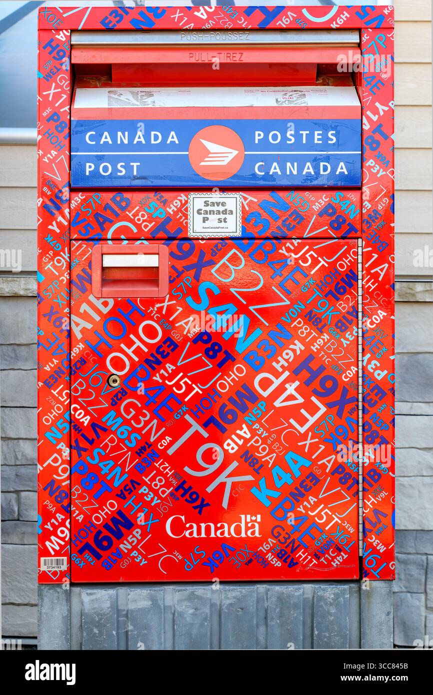 Saint John, NB, Canada - September 30, 2024: A Canada Port mailbox stands outdoors. The mailbox is covered with fragments of postal codes. Closeup. Stock Photo