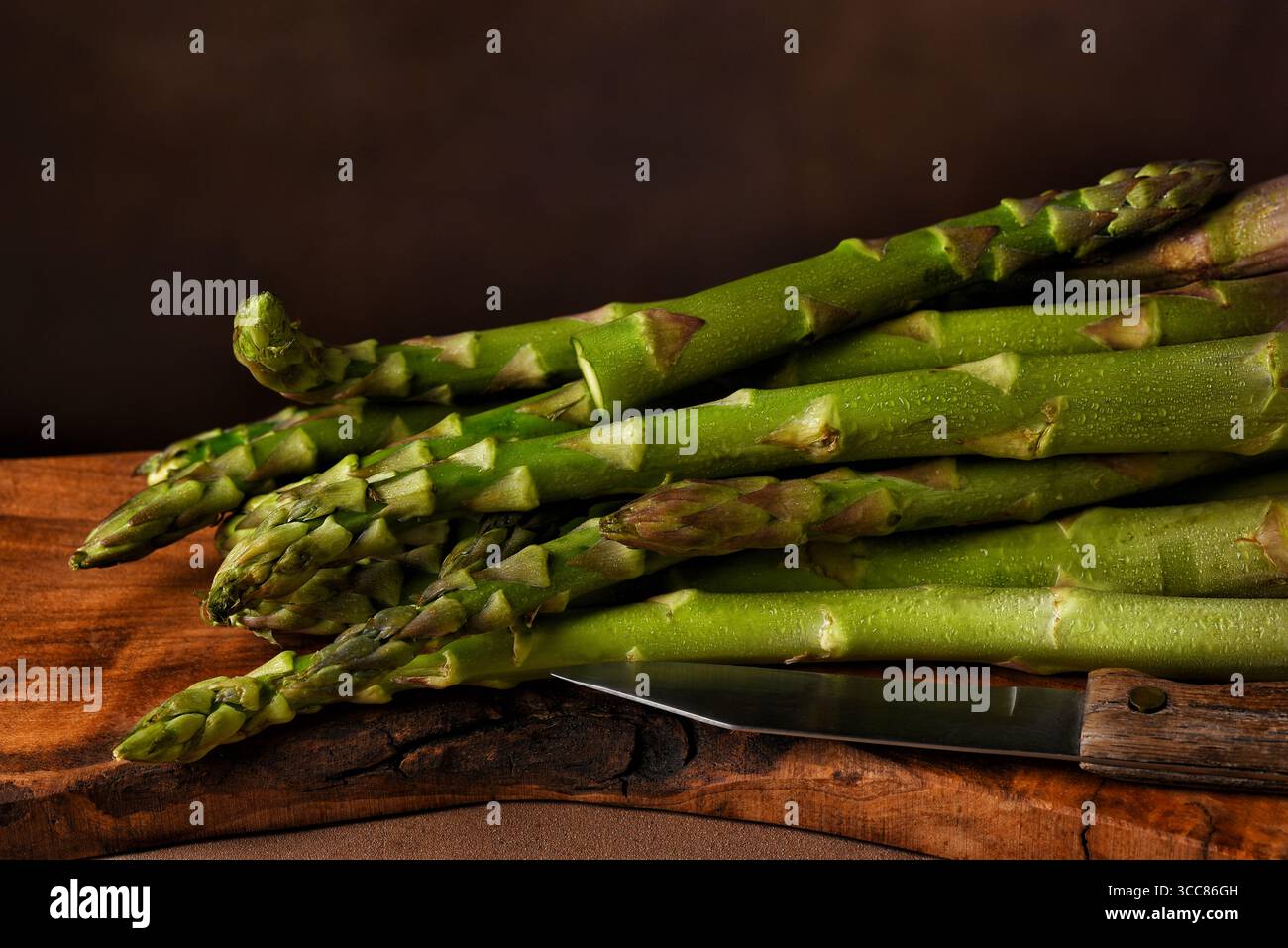 A bunch of Asparagus on a wooden cutting board with knife. Stock Photo
