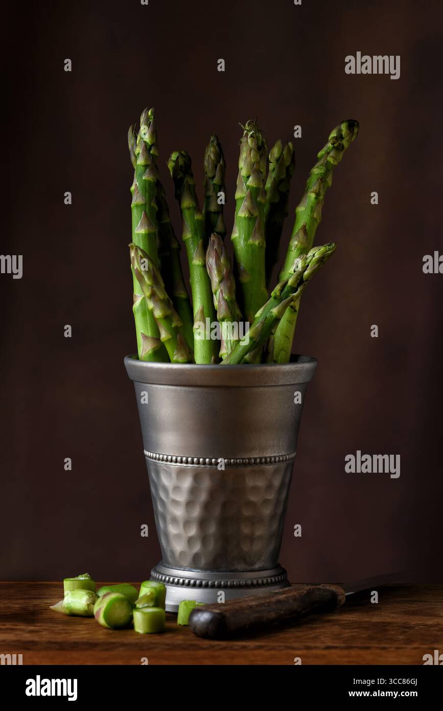 A pewter cup filled with Asparagus Spears on a rustic wood table and a warm mottled background. Stock Photo