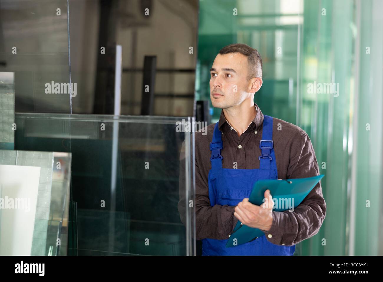 Focused technician inspecting and documenting glass panels in workshop Stock Photo