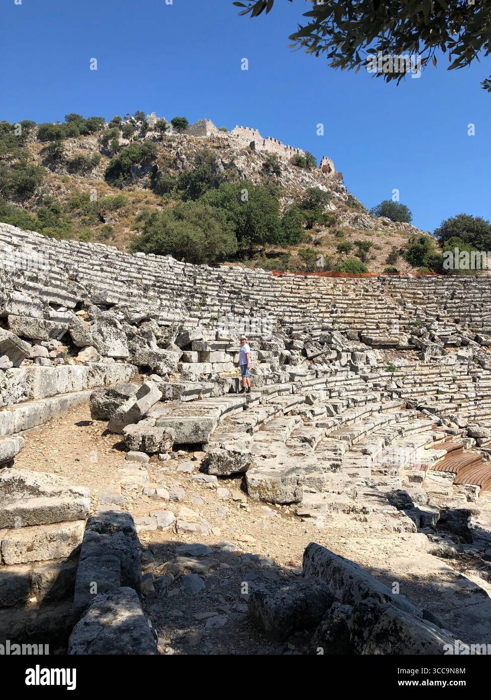Ancient stone amphitheater with tiered seating, set against a backdrop of a rocky hillside under a clear blue sky. - Smartphone Captured Stock Image