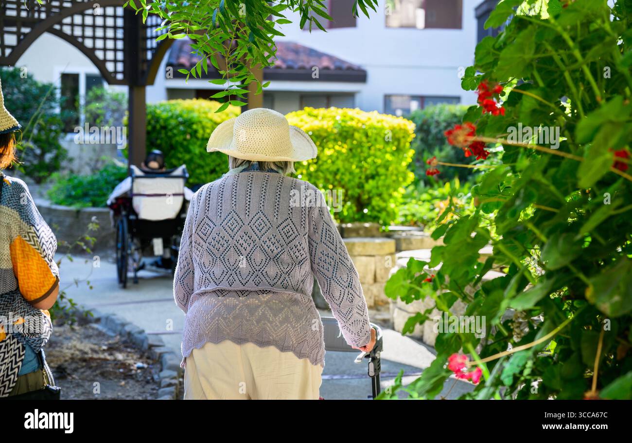 Elderly woman walking using a mobility walker with her adult daughter ...