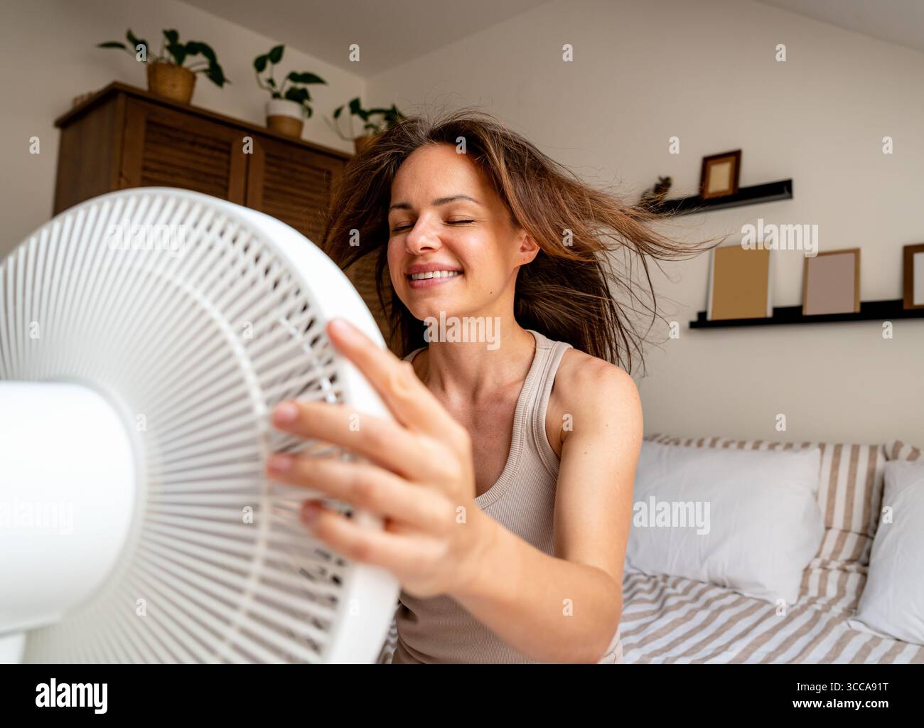 Smiling woman enjoying cool breeze from electric fan on hot summer day Stock Photo