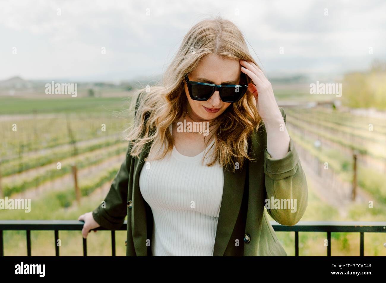 Woman in sunglasses poses confidently at vineyard railing Stock Photo
